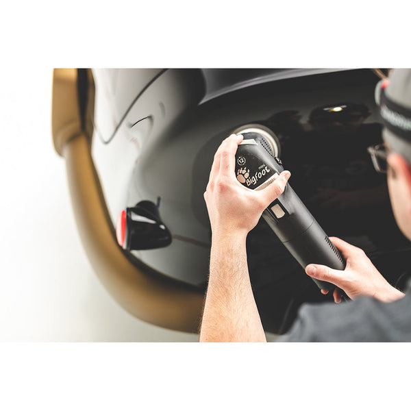 A closeup of a person polishing a black car with a Rupes polisher.