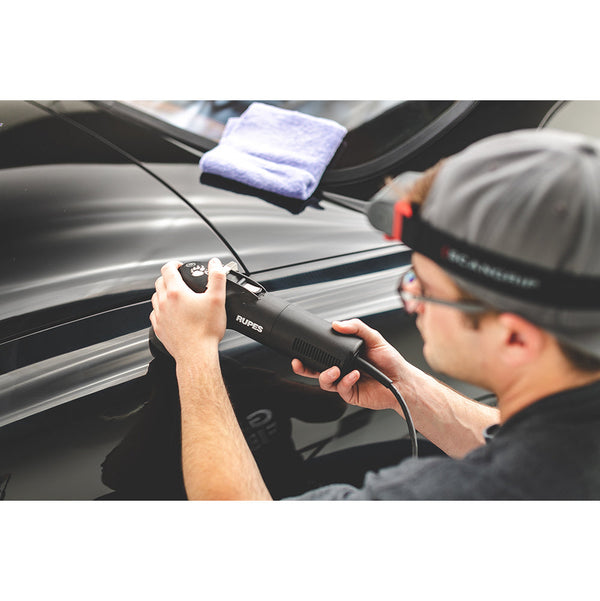 A closeup of a person polishing a black car with a Rupes polisher.