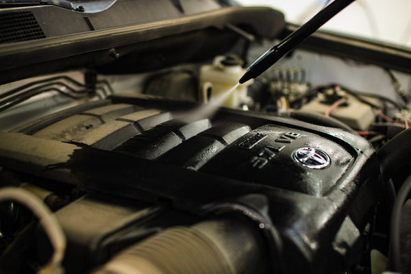 A person cleaning the engine of a car with The Rag Company Ultra Air Engine Blaster.