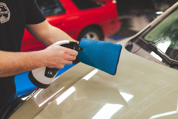 A person spraying into a blue Ultra Clay Mitt with a spray bottle.