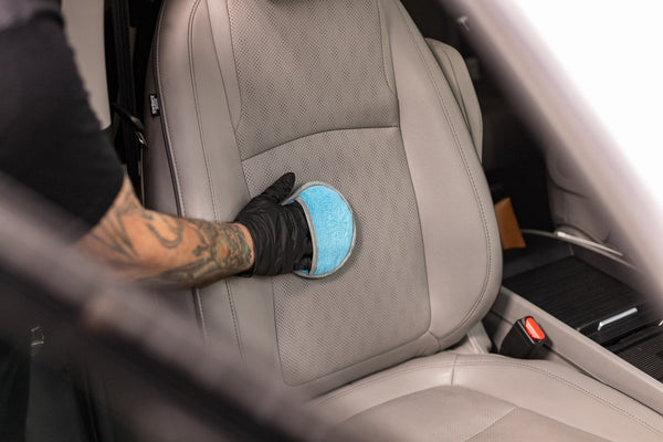 A person using the Ultra No Soak Round Detailing Applicator to scrub a seat inside of a car.