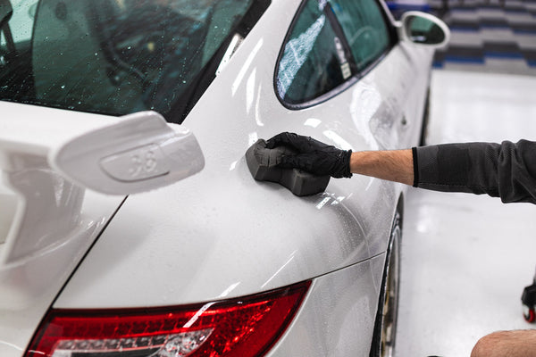 A person scrubbing a white car with a TRC Ultra Safe Sponge.