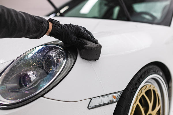 A person scrubbing a white car with a TRC Ultra Safe Sponge.