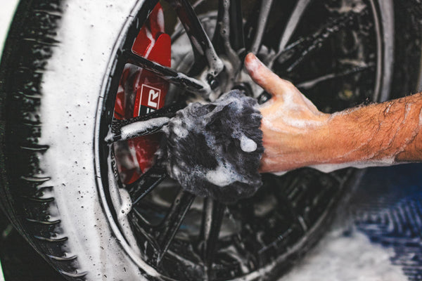 A person washing a wheel with the Wool Wheel Mitt.