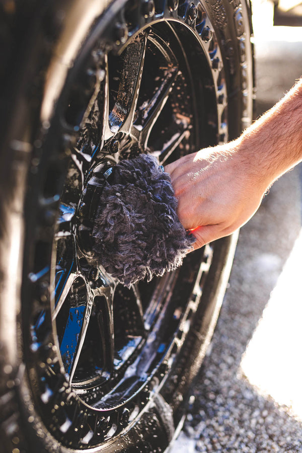 A person washing a wheel with the Wool Wheel Mitt.