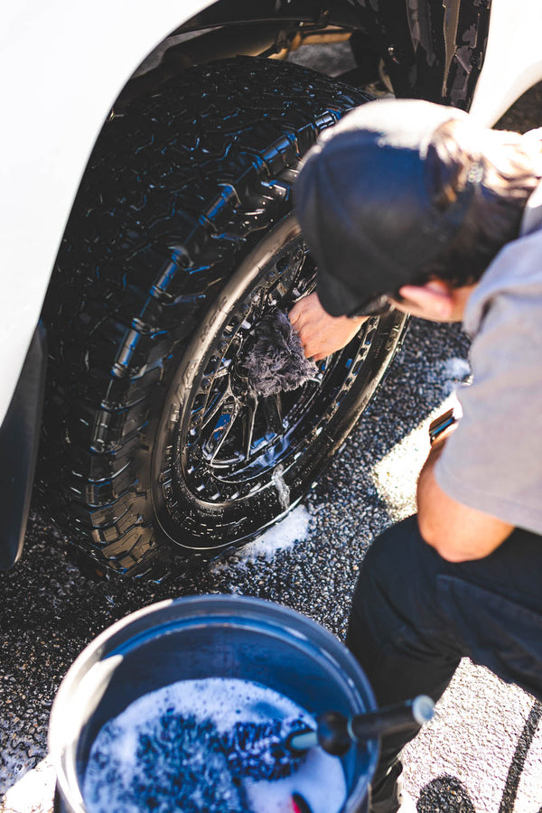 A person washing a wheel with the Wool Wheel Mitt.