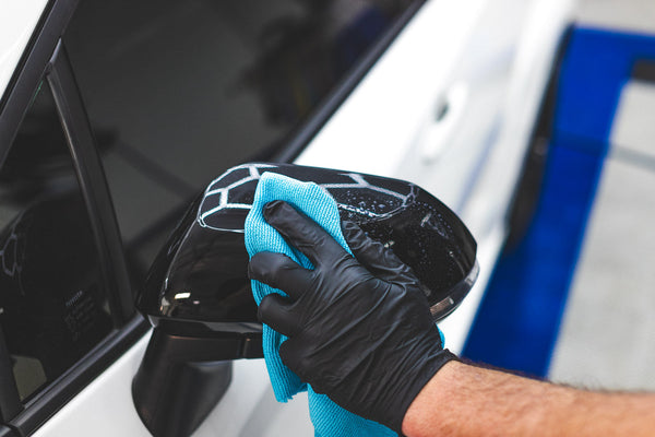 A person wearing black rubber gloves cleaning off the side mirrors of a black car with the Ultra Rip N Rag.